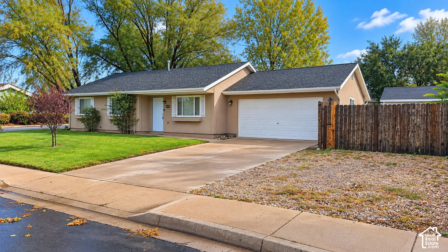 Single-story residence featuring a neutral stucco exterior, an attached two-car garage, white window shutters, and a wood-slat privacy fence