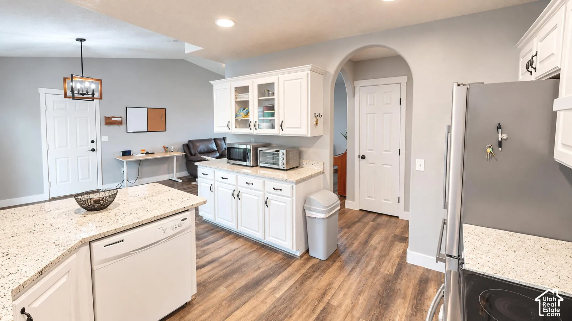 Kitchen featuring white cabinetry with glass-front uppers, speckled stone-finish countertops, wood-finish flooring, a farmhouse-style pendant light, and an architectural arched entryway