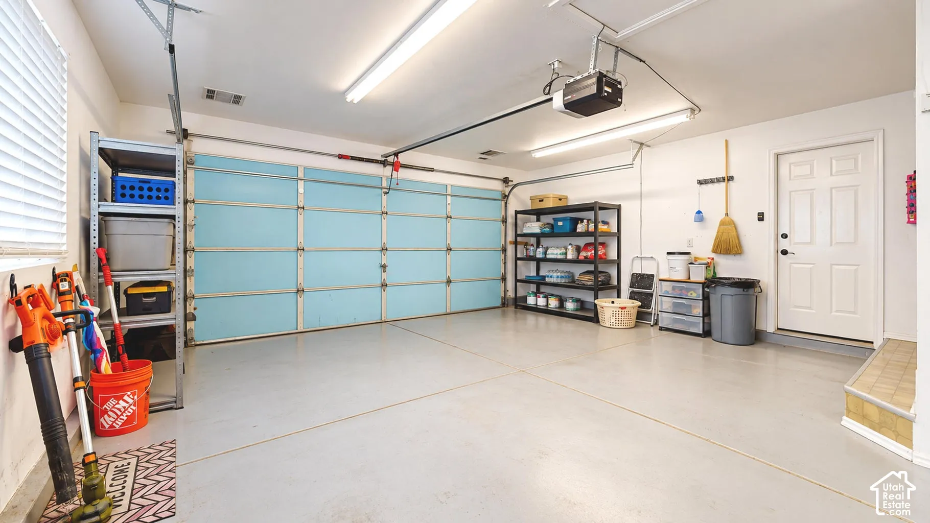 Attached two-car garage featuring a sectional door, dual fluorescent lighting fixtures, smooth-finish concrete flooring, and a dedicated side entry door