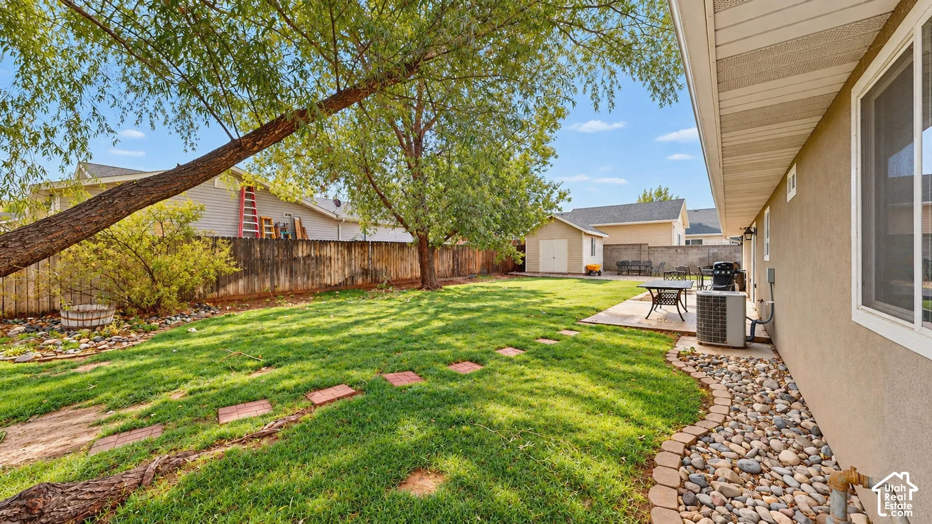 Backyard featuring a manicured lawn, stone paver pathway, detached storage shed, perimeter wood fencing, and mature trees