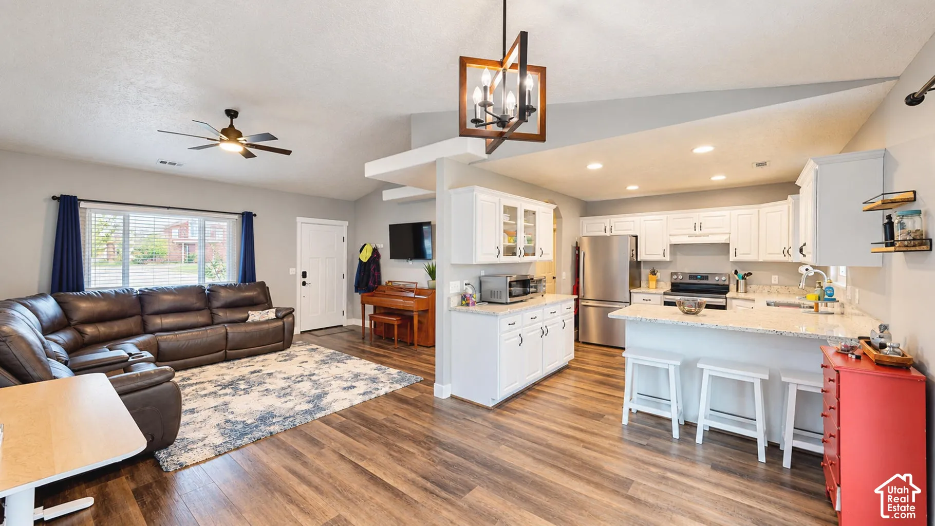Open-concept space featuring vaulted ceilings, wood-finish flooring, white cabinetry with speckled stone countertops, a geometric chandelier, and recessed lighting