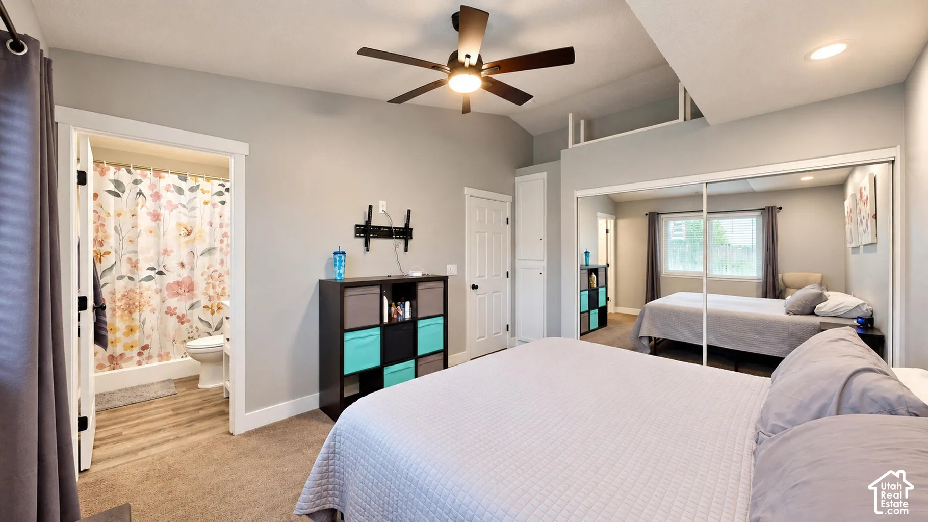 Vaulted ceilings with a central lighted ceiling fan, wall-to-wall carpeting, floor-to-ceiling mirrored closet doors, and built-in vertical storage cabinetry