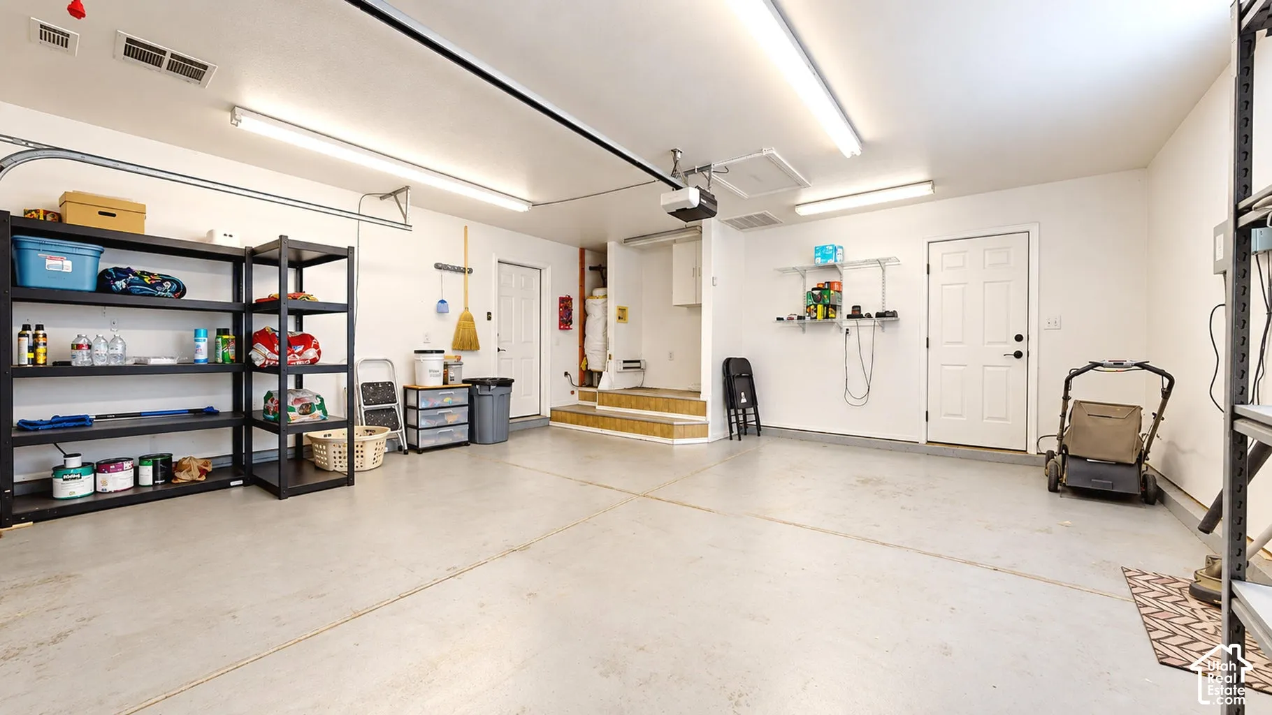 Multi-car garage featuring painted concrete flooring, overhead fluorescent lighting, an automated garage door opener, and two interior entry doors