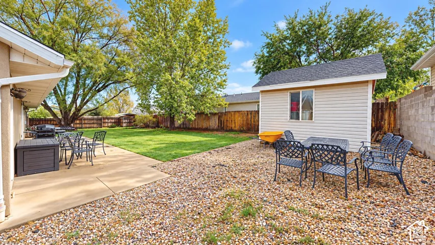 Backyard featuring a concrete patio, gravel hardscaping, detached structure, wood fencing, and mature trees