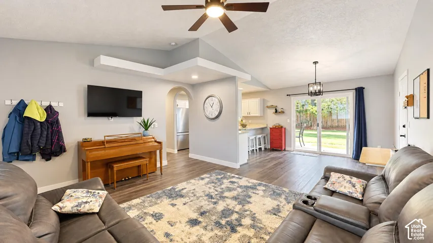 Vaulted ceilings, wood-finish flooring, sliding glass patio doors, kitchen peninsula with breakfast bar seating, and arched doorway