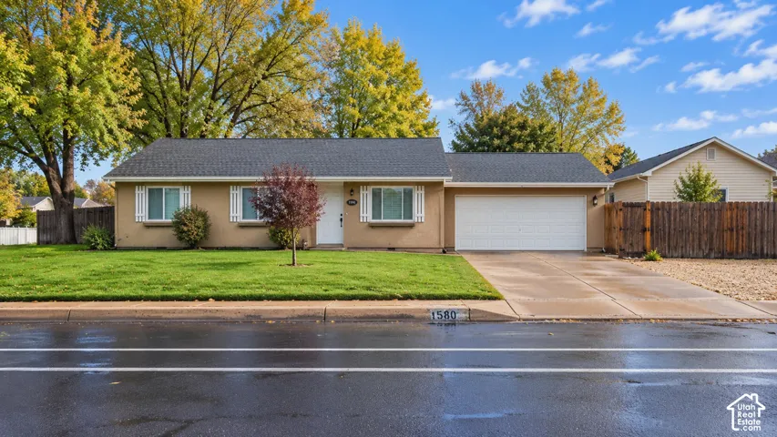 Single-story exterior featuring a light-toned stucco facade, dual front-facing windows with white shutters, a multi-car attached garage, and an expansive front lawn