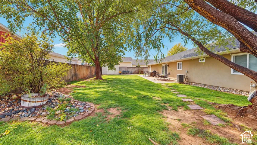 Backyard featuring a grass lawn, paved stone patio, perimeter block wall, stone-bordered landscaping, and mature trees