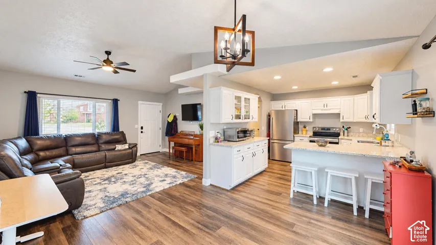 Open-concept space featuring vaulted ceilings, wood-finish flooring, white cabinetry with speckled stone countertops, a geometric chandelier, and recessed lighting