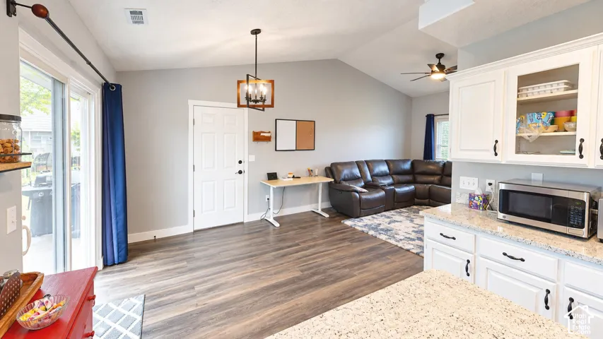 Vaulted ceilings, wood-finish flooring, white cabinetry, stone-finish countertops, and hanging geometric pendant lighting