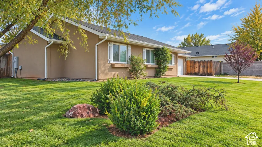 Stucco exterior featuring window shutters, a concrete driveway, a wood fence, and landscaped shrubbery