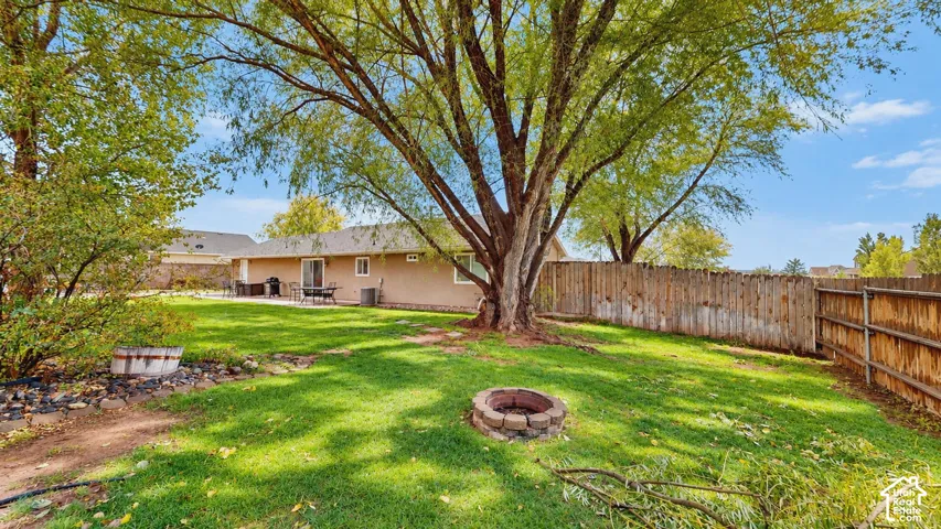 Backyard featuring mature trees, a stone fire pit, wood fencing, and a concrete patio