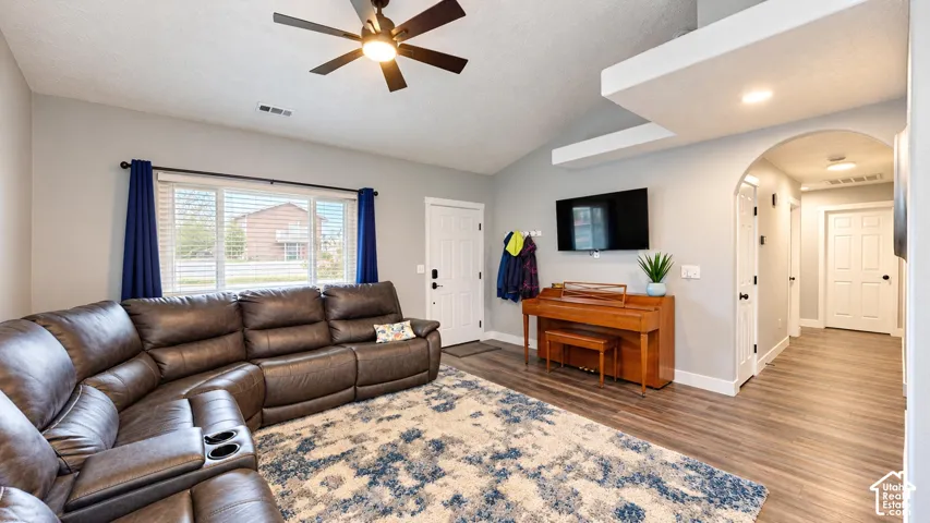 Living area featuring vaulted ceilings, wood-finish flooring, a ceiling fan with integrated lighting, and an arched entryway