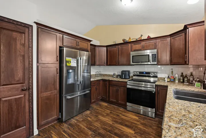 Kitchen featuring stained wood cabinetry, stone-finish countertops, stainless steel appliances, white subway tile backsplash, and wood-finish flooring