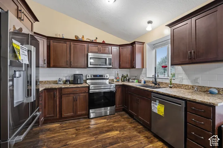 Kitchen featuring dark wood cabinetry, stone countertops, white subway tile backsplash, stainless steel appliances, and wood-finish flooring