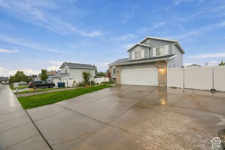 Two-story residence featuring horizontal vinyl siding, stone veneer accents, a multi-car concrete driveway, an attached garage, and white vinyl privacy fencing