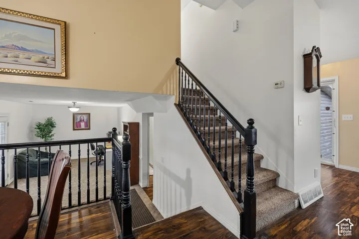 Staircase featuring carpeted treads, dark wood-finish handrails, and black balusters, complemented by dark wood-finish flooring