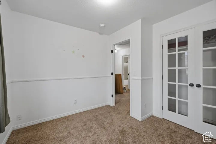 Interior room featuring neutral wall-to-wall carpeting, white chair rail molding, and double French doors with glass panes