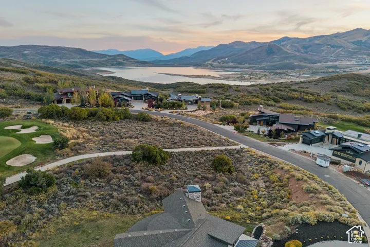Expansive property featuring a golf course, paved roads, and distant lake with mountain backdrops
