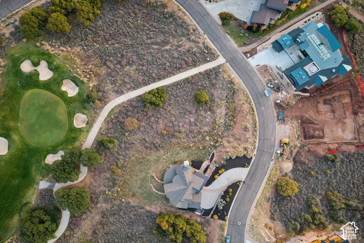 Curved asphalt roadway, golf course green with sand traps, and natural landscaping with mature trees