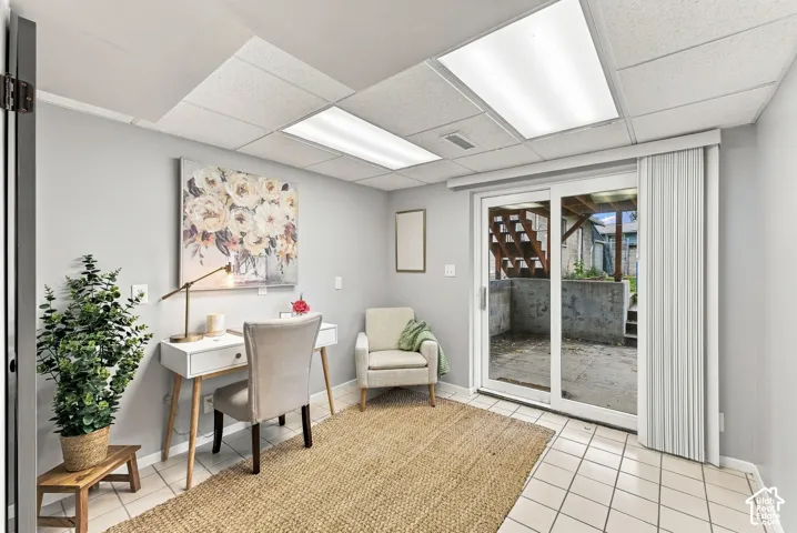 Room featuring light-colored tile flooring, drop ceiling with integrated rectangular lighting, and sliding glass doors with vertical blinds