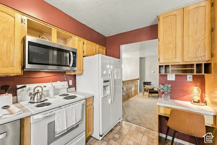 Kitchen featuring light wood cabinetry, integrated microwave, white appliances, tiled flooring, and built-in desk area