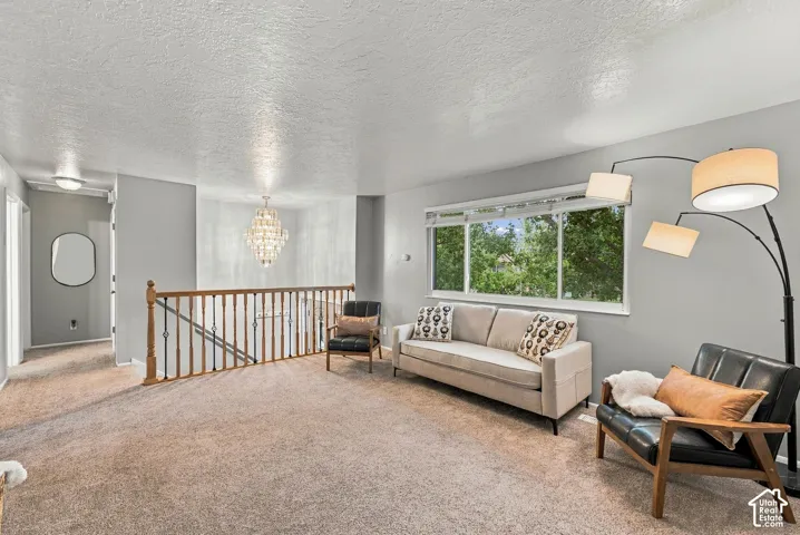 Open-concept interior featuring wall-to-wall carpeting, wood-and-metal stair railing, multi-pane window, and decorative multi-tiered pendant light fixture