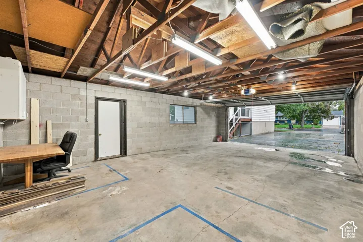 Garage space featuring exposed beam ceiling construction, concrete block walls, concrete flooring, and linear fluorescent lighting fixtures