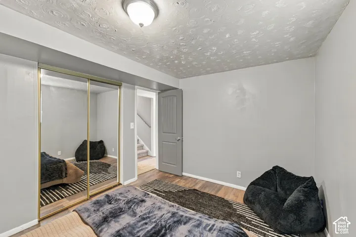 Interior room featuring wood-finish flooring, textured ceiling, sliding mirrored closet doors with metallic trim, and a raised-panel interior door