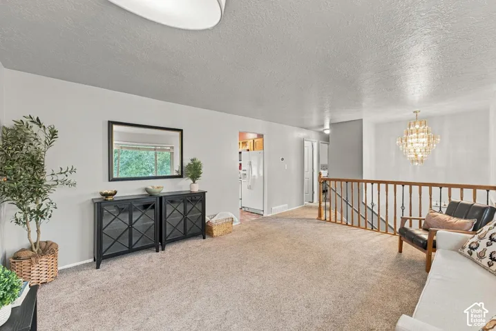 Neutral-toned interior featuring wall-to-wall carpeting, wood-finish balustrade, and tiered crystal chandelier lighting