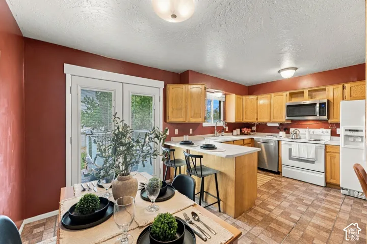 Kitchen featuring wood cabinetry, stainless steel appliances, a peninsula with counter seating, and tile flooring, including glass-panel double doors