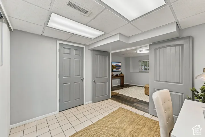 Room featuring neutral-toned walls, tile flooring, grey six-panel interior doors, and recessed drop-ceiling lighting