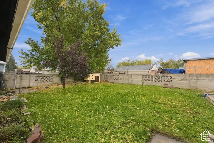 Backyard featuring a grass lawn, decorative concrete block perimeter fencing, mature trees, and stone-bordered landscaping beds