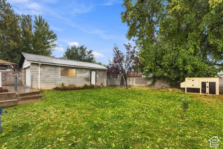 Detached concrete block garage featuring a metal roof, concrete patio steps, perimeter masonry wall, and a grass-covered lot