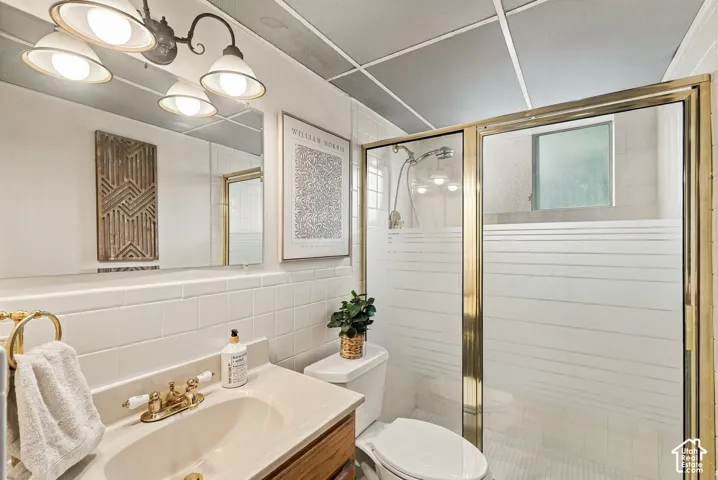 Bathroom featuring white wall tile, a metallic-framed glass shower enclosure, vanity with an integrated sink, three-light wall-mounted fixture, and a large mirror