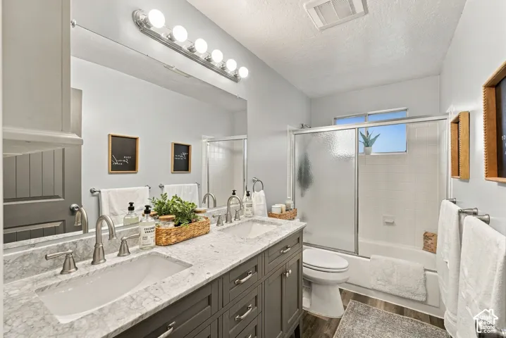 Double vanity featuring gray cabinetry, stone-finish countertops, undermount sinks, satin nickel hardware, and a glass-enclosed tub and shower combination