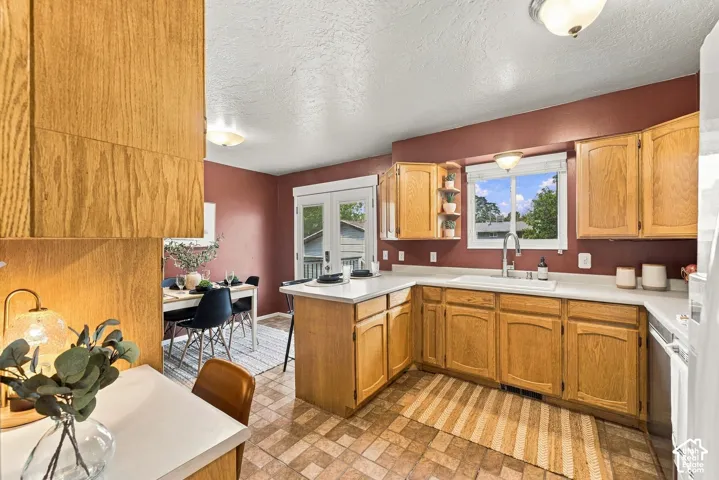 Kitchen featuring natural wood cabinetry, solid surface countertops, an integrated white sink with a high-arch faucet, and double glass-paned exterior doors