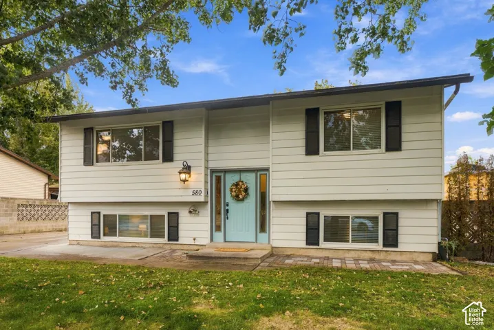 Split-level exterior featuring horizontal siding, dark decorative window shutters, a central entrance with sidelights, and a paver stone walkway
