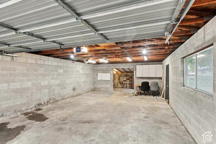 Garage featuring exposed wood ceiling joists, concrete block walls, concrete flooring, and wall-mounted storage cabinetry