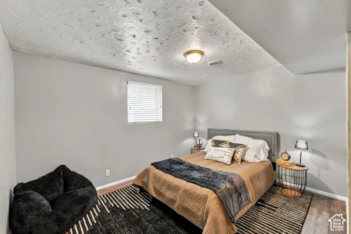 Room featuring a textured ceiling, neutral walls, wood-finish flooring, and a single window with blinds