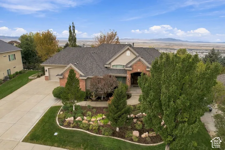 Brick and stucco exterior featuring an arched entryway, gabled roofline, multi-car garages, and landscaped front yard with mature trees and stone hardscaping
