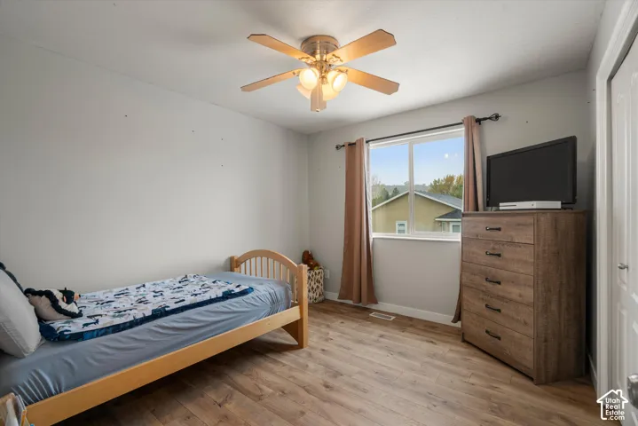Room featuring wood-finish flooring, a neutral wall palette, a multi-light ceiling fan, and a window with horizontal trim