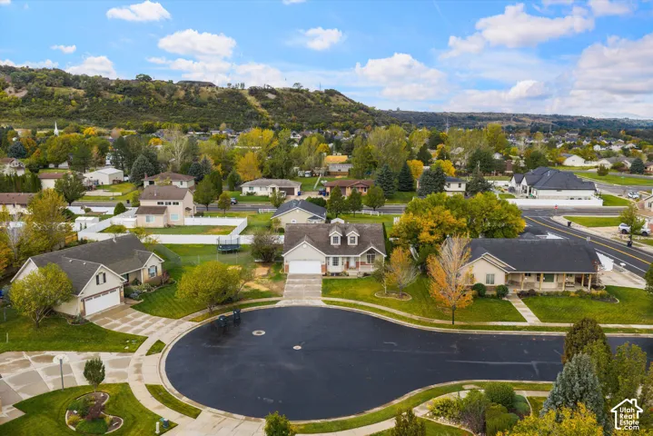Aerial view of a residential cul-de-sac featuring single-family homes, concrete driveways, manicured lawns, and a backdrop of hillside terrain