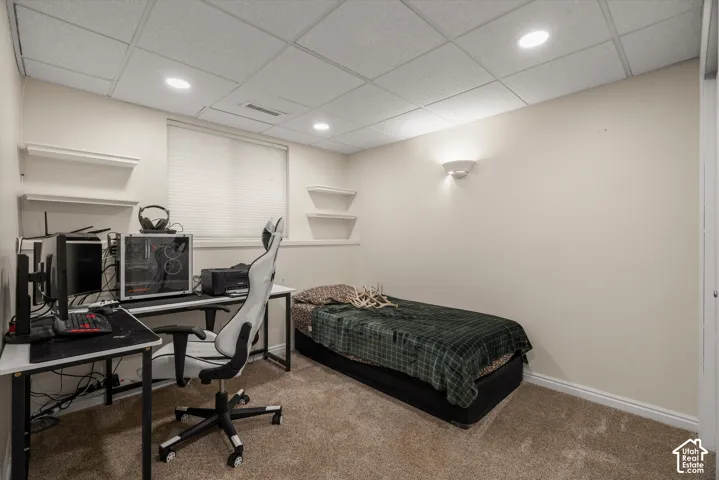 Room featuring wall-to-wall carpeting, a drop ceiling with recessed lighting, integrated wall sconce, and built-in wall shelving