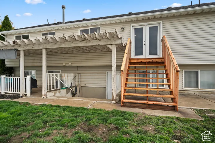 Exterior features a pergola-covered patio, concrete hardscaping, double glass-panel doors, and an elevated wood staircase with matching railing