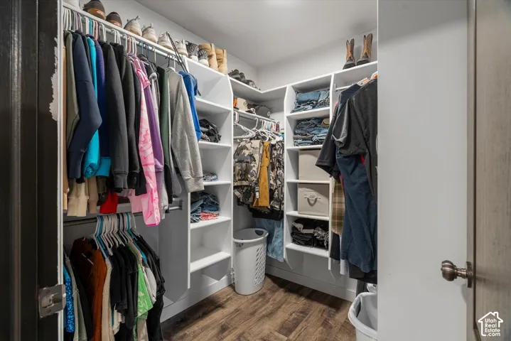 Walk-in closet featuring white custom built-in shelving, hanging rods, and wood-finish flooring