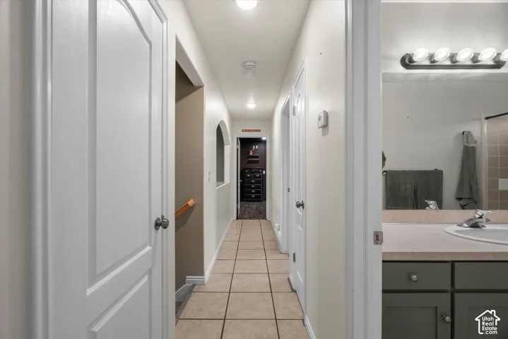 Hallway featuring ceramic tile flooring, arched wall detail, and multiple interior doors with metal hardware, paired with a bathroom vanity containing an integrated sink and multi-light fixture