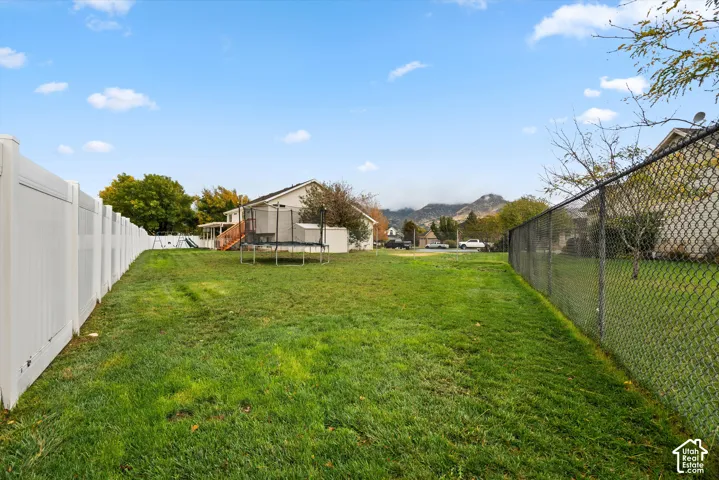 Expansive backyard featuring a manicured lawn, white vinyl perimeter fencing, and chain-link side fencing with mountain backdrop