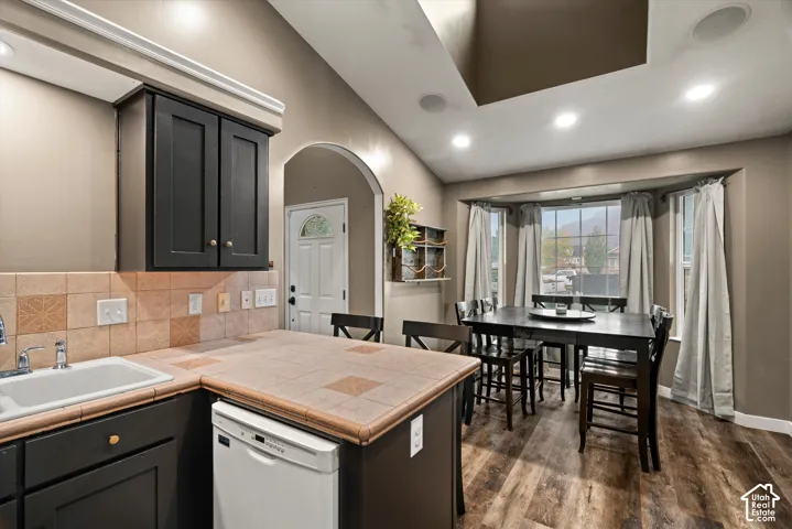 Kitchen featuring tile countertops, dark cabinetry, wood-finish flooring, recessed lighting, and a bay window