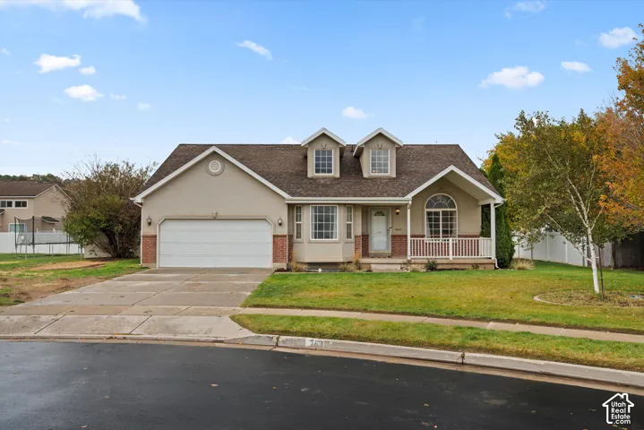 Multi-level exterior featuring brick and stucco siding, a two-car garage, dual roof dormers, a covered front porch with a railing, and a bay window