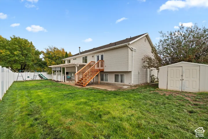 Exterior rear elevation featuring light-colored horizontal siding, an elevated wooden deck with stairs, a ground-level concrete patio, and a detached storage shed